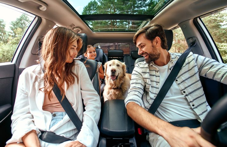 Familia sonriendo dentro de su auto con su perro