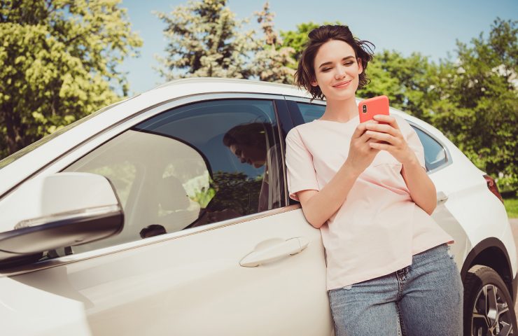Mujer sonriendo con su celular junto a su auto