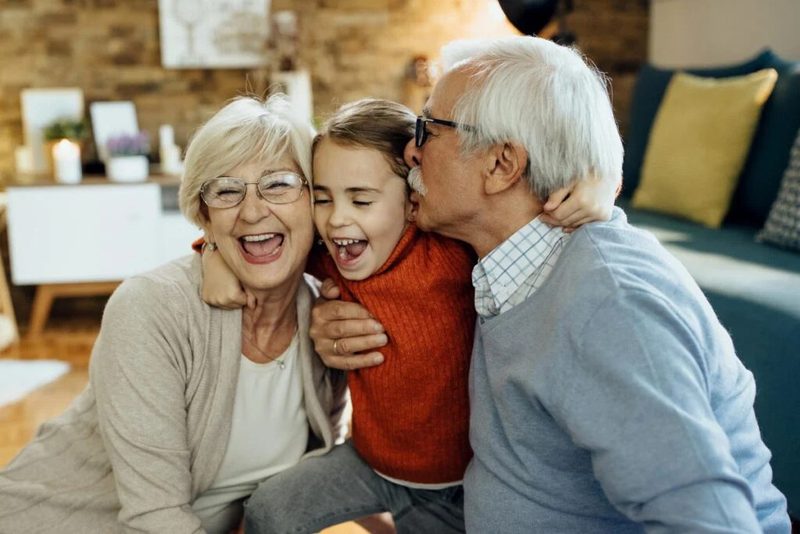 Abuelos abrazando a su nieta, riendo en casa